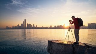 Best budget tripods: Photographer with camera on tripod photographing urban skyline at sunrise. Abu Dhabi, United Arab Emirates.